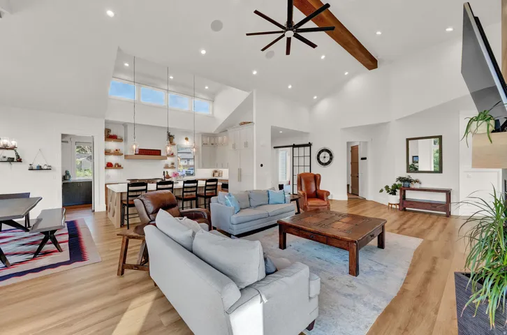Living area featuring beamed ceiling, light wood-style floors, a barn door, healthy amount of natural light, and high vaulted ceiling