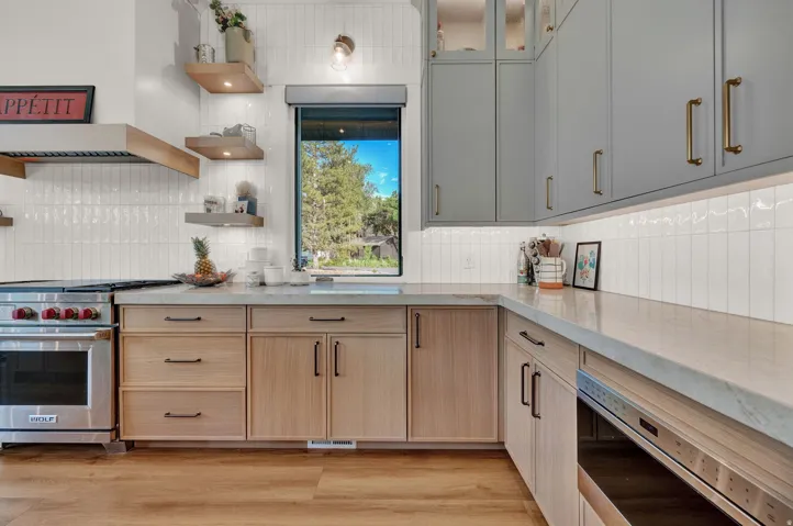 Kitchen with appliances with stainless steel finishes, custom range hood, light brown cabinetry, glass insert cabinets, and light wood-style flooring