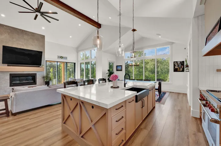 Kitchen featuring a tile fireplace, high vaulted ceiling, light brown cabinets, light stone countertops, and range with two ovens