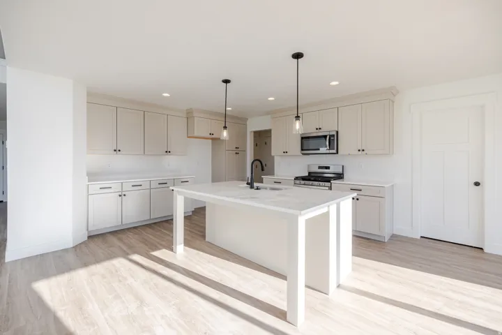Kitchen with light wood finished floors, stainless steel appliances, a center island with sink, a breakfast bar, and decorative light fixtures