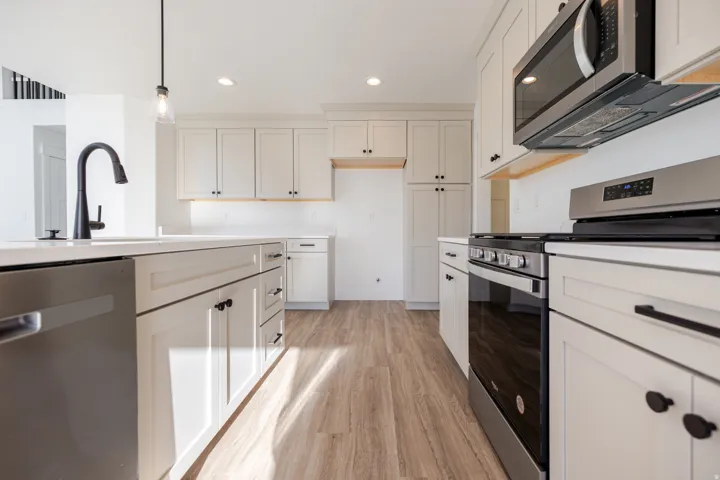 Kitchen with stainless steel appliances, light wood-style floors, pendant lighting, and white cabinetry