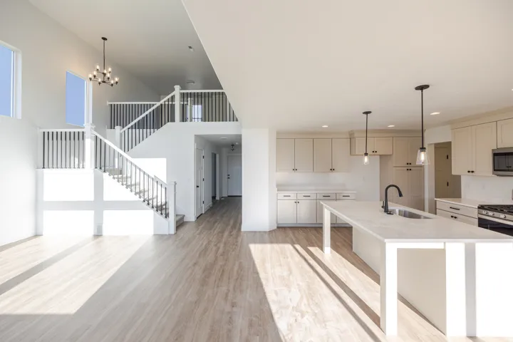 Kitchen featuring light wood finished floors, stainless steel microwave, a center island with sink, light stone counters, and hanging lights