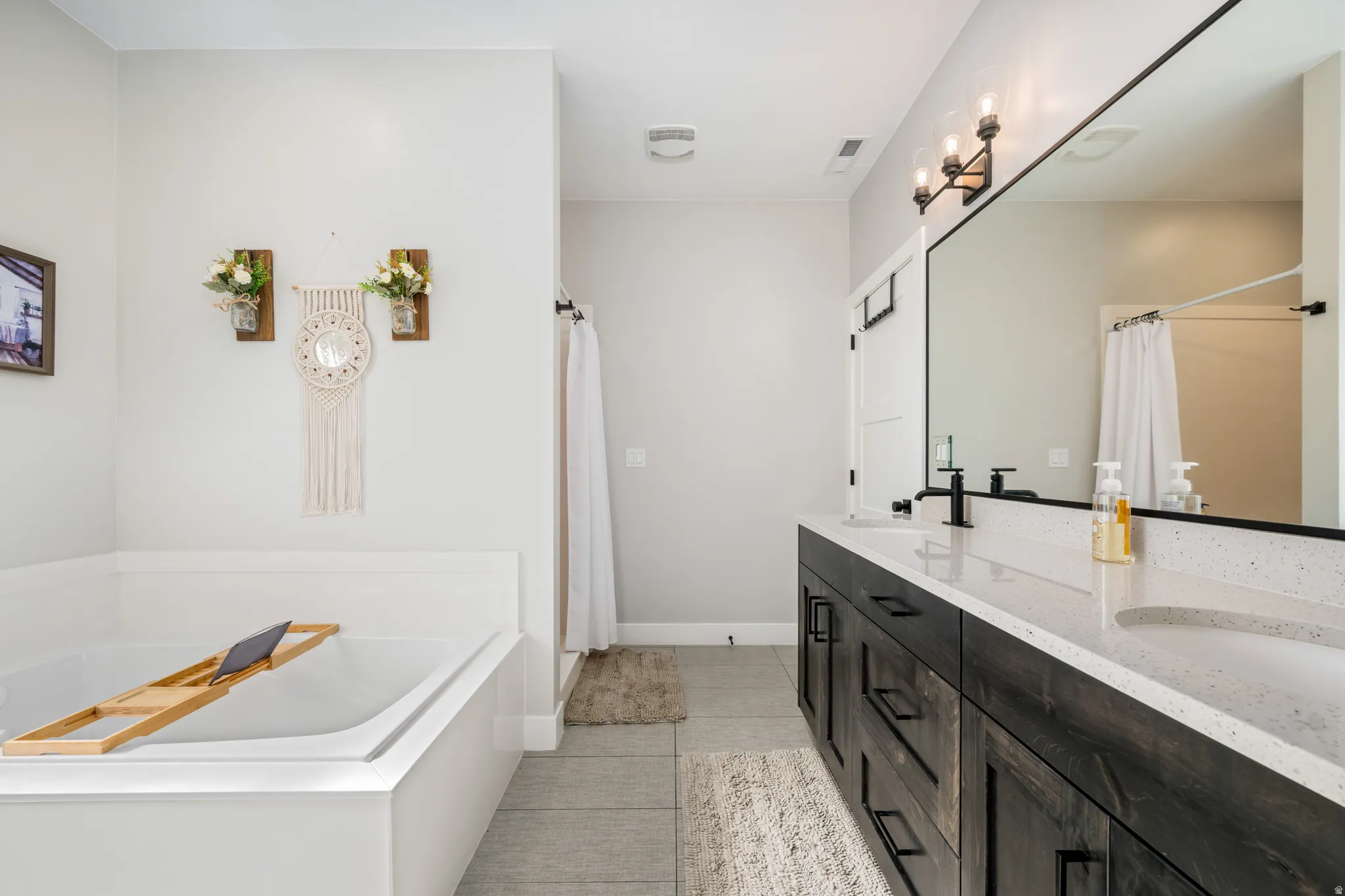 Bathroom with a bath, double vanity, light tile patterned floors, and curtained shower