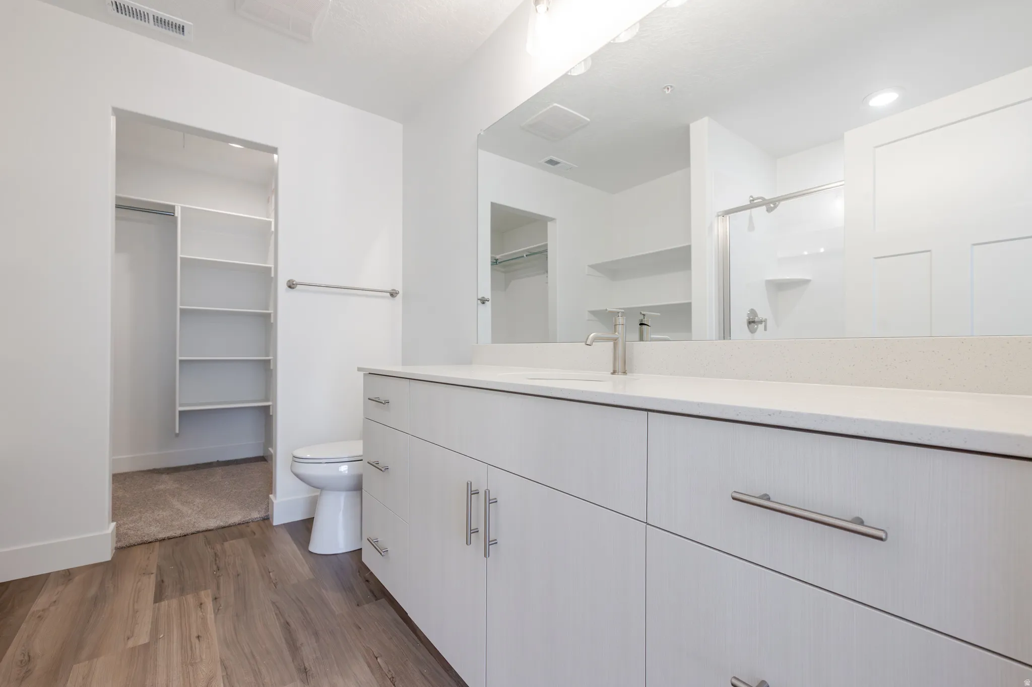 Full bath featuring a spacious closet, a stall shower, vanity, and dark wood finished floors