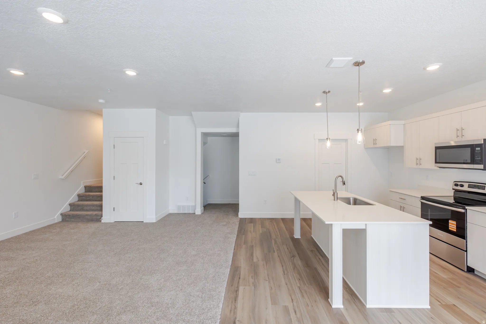 Kitchen featuring stainless steel appliances, pendant lighting, a kitchen bar, an island with sink, and a textured ceiling