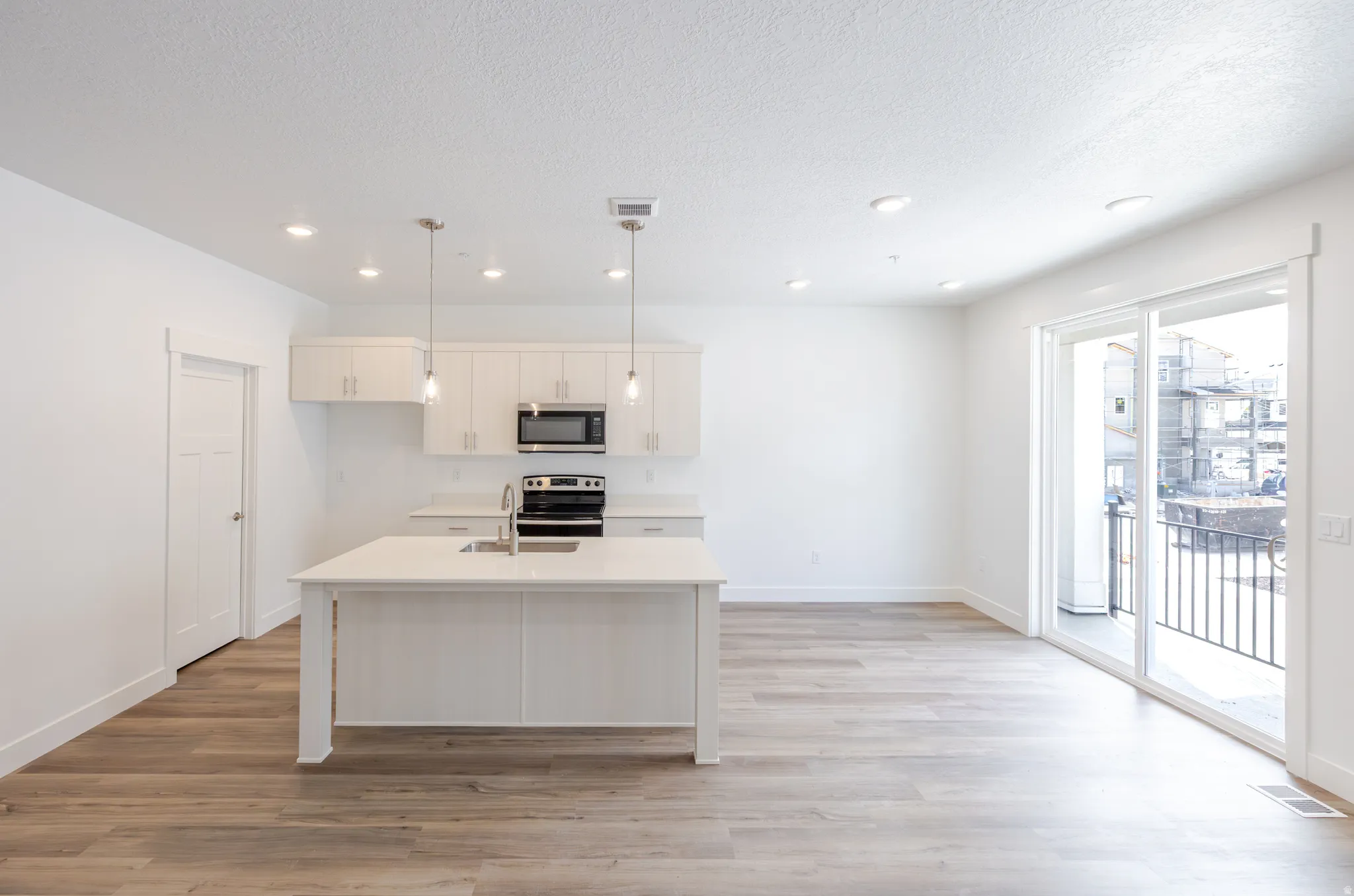 Kitchen featuring an island with sink, pendant lighting, light wood-style floors, stainless steel appliances, and a textured ceiling