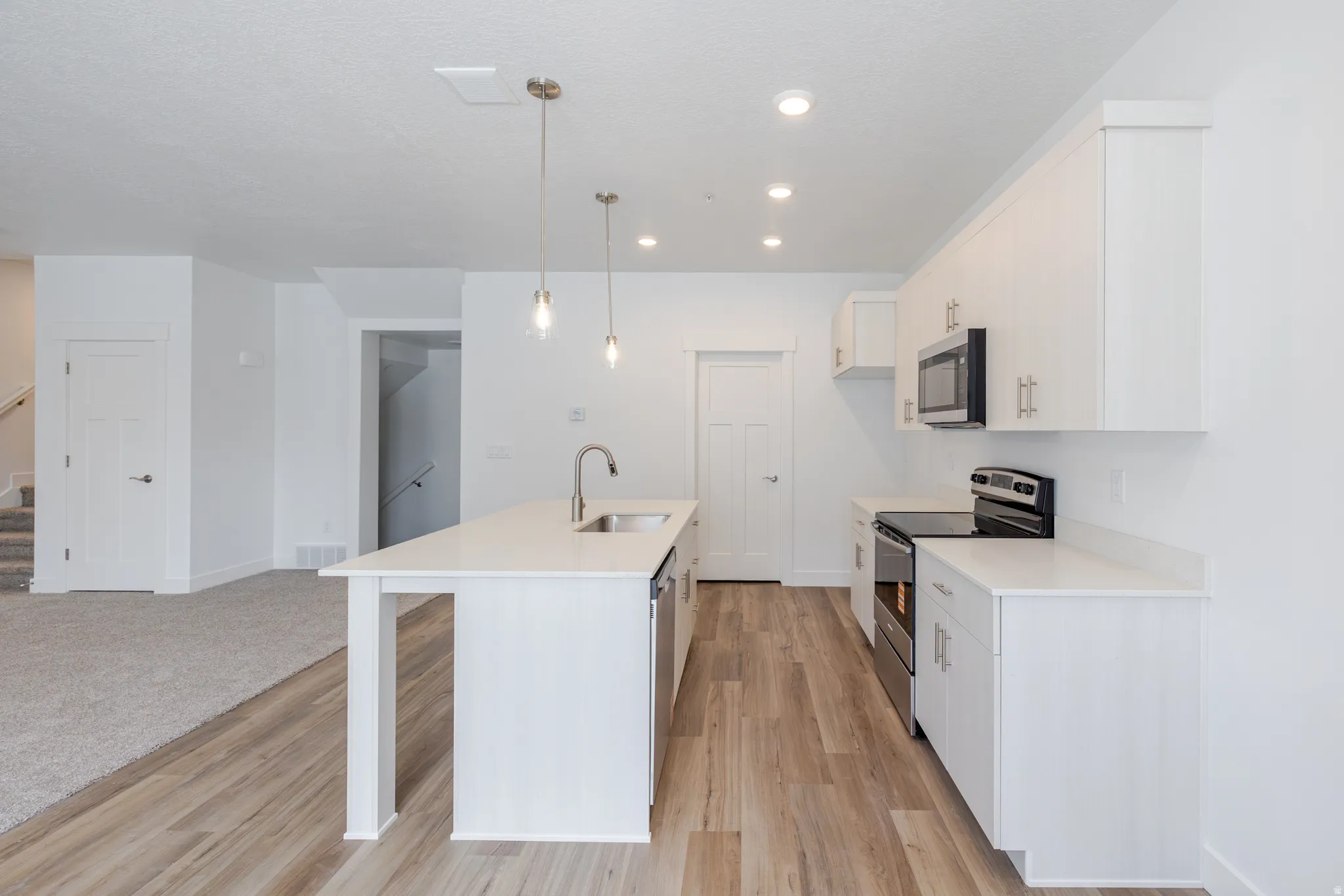 Kitchen with stainless steel appliances, an island with sink, hanging light fixtures, a kitchen bar, and light wood-style flooring