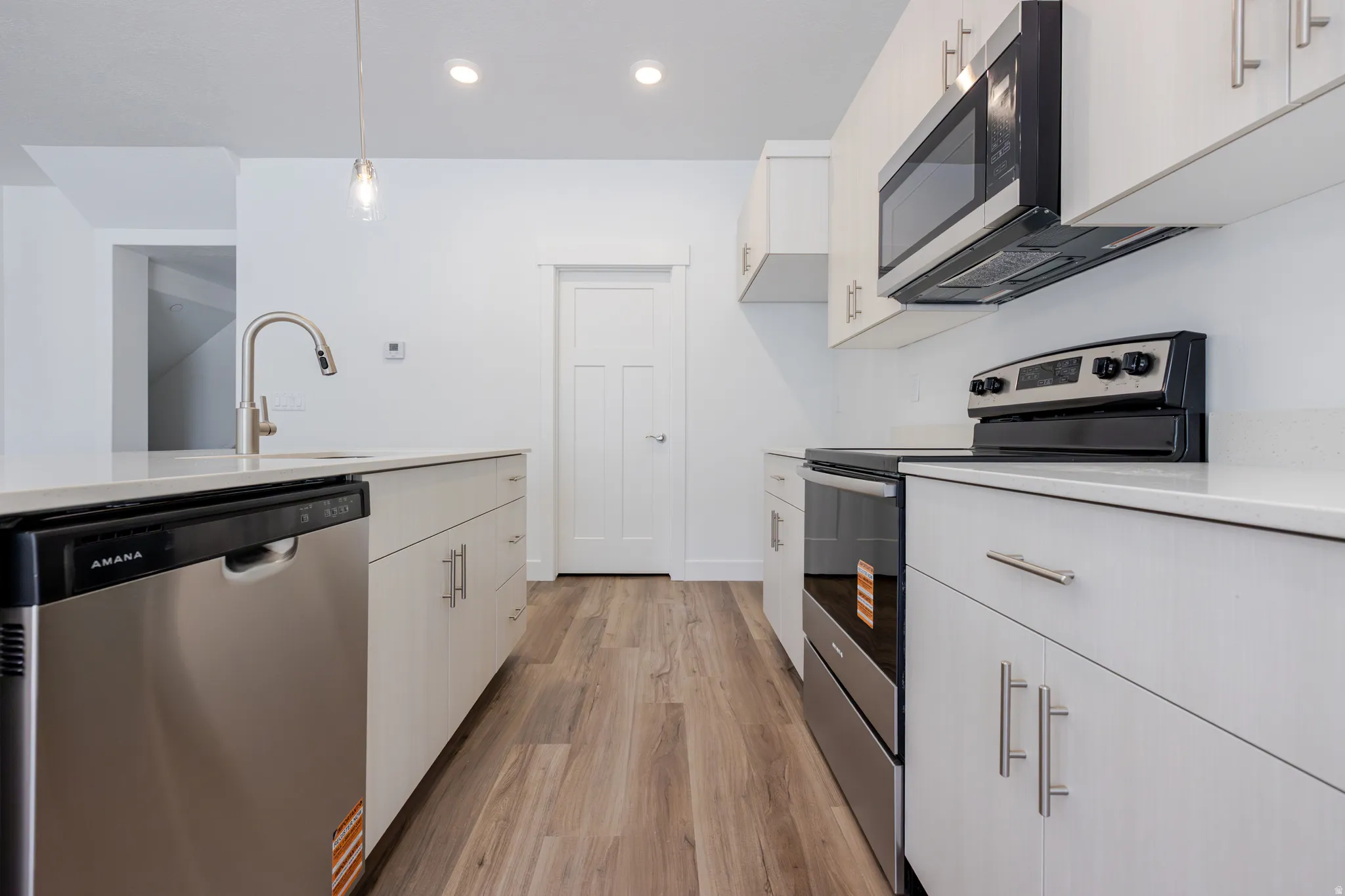 Kitchen featuring stainless steel appliances, light wood-type flooring, pendant lighting, and light stone counters