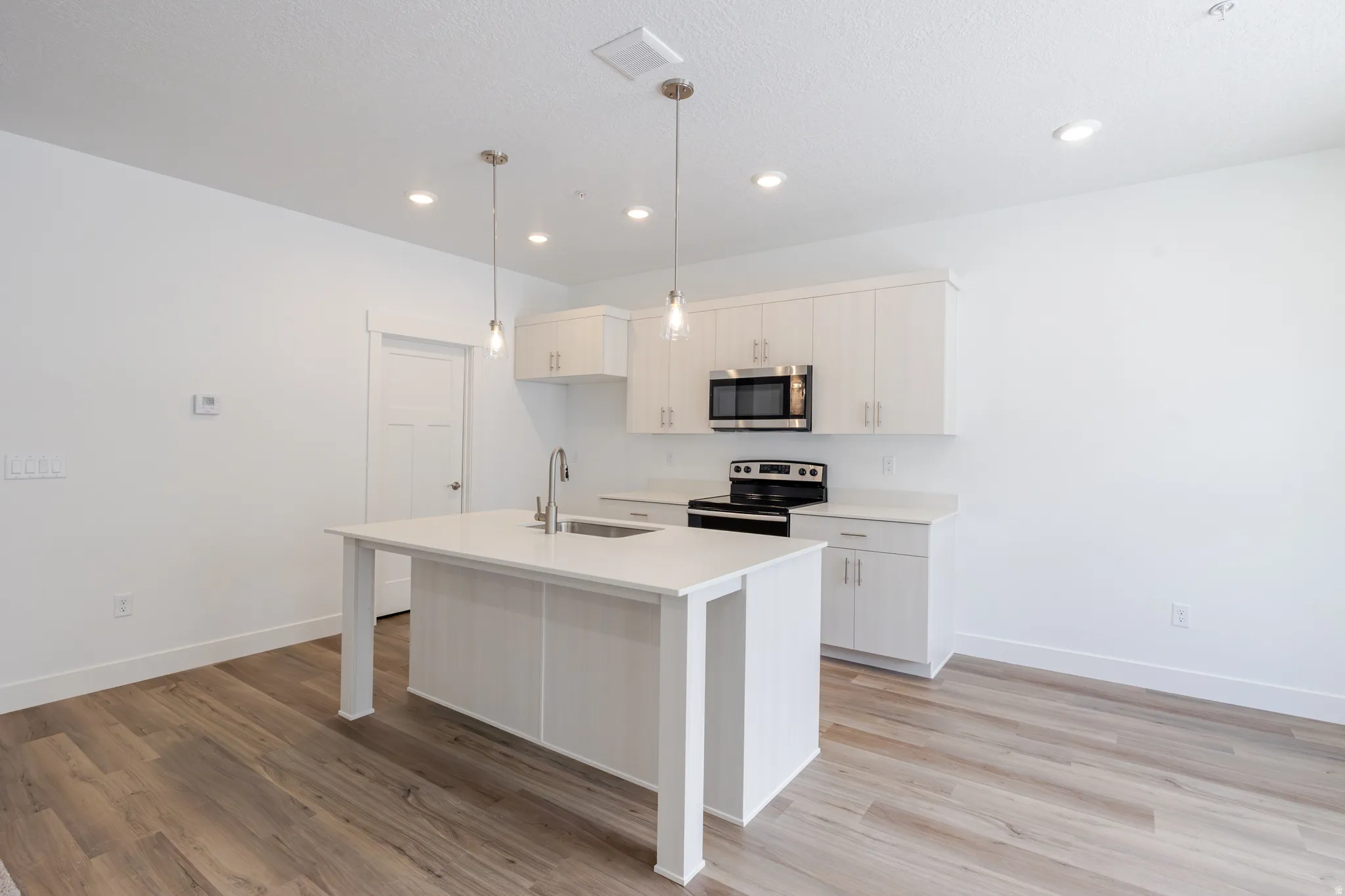 Kitchen featuring stainless steel appliances, decorative light fixtures, an island with sink, light wood-style flooring, and a kitchen breakfast bar