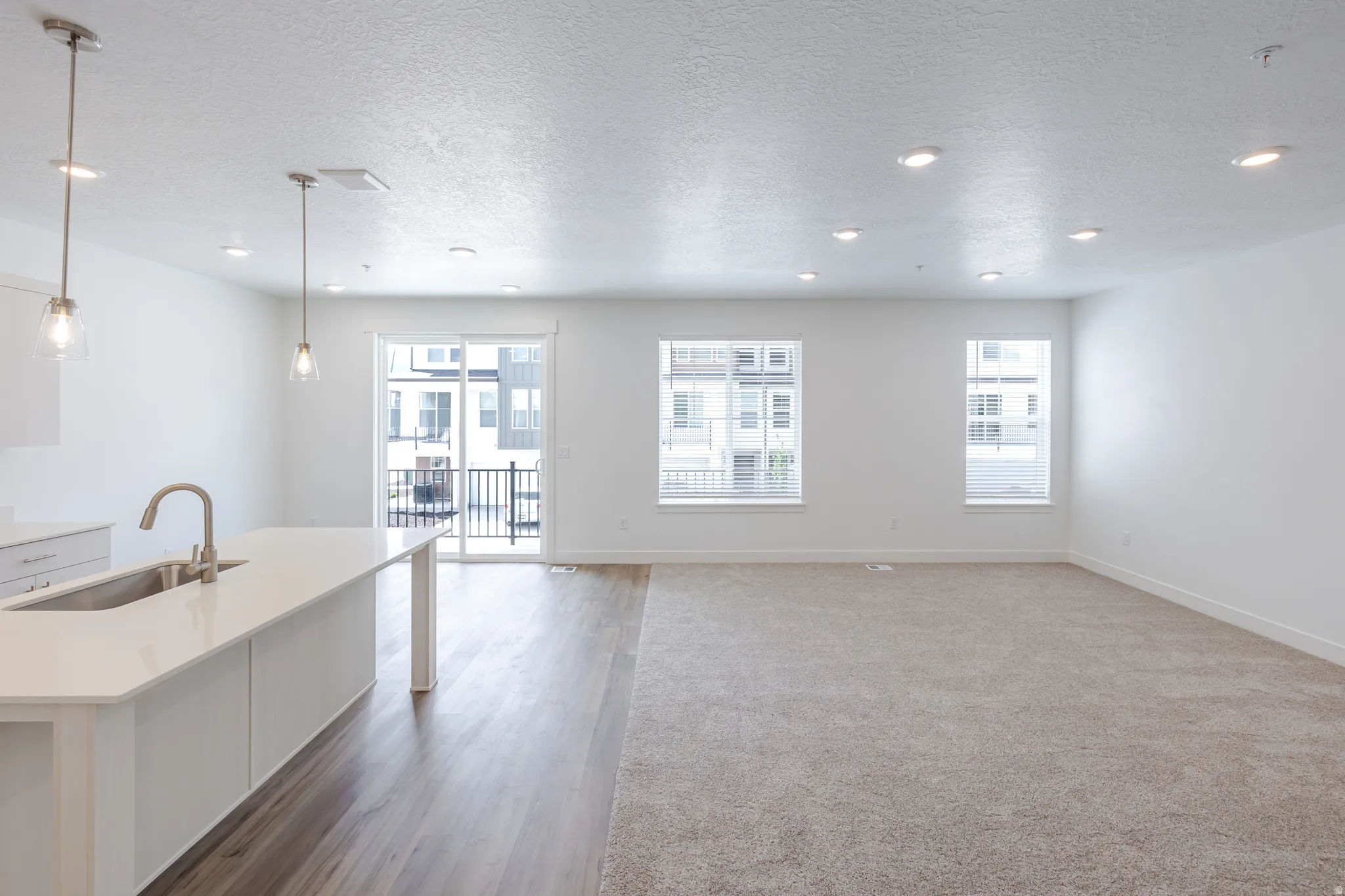 Kitchen featuring a center island with sink, a textured ceiling, white cabinets, pendant lighting, and open floor plan