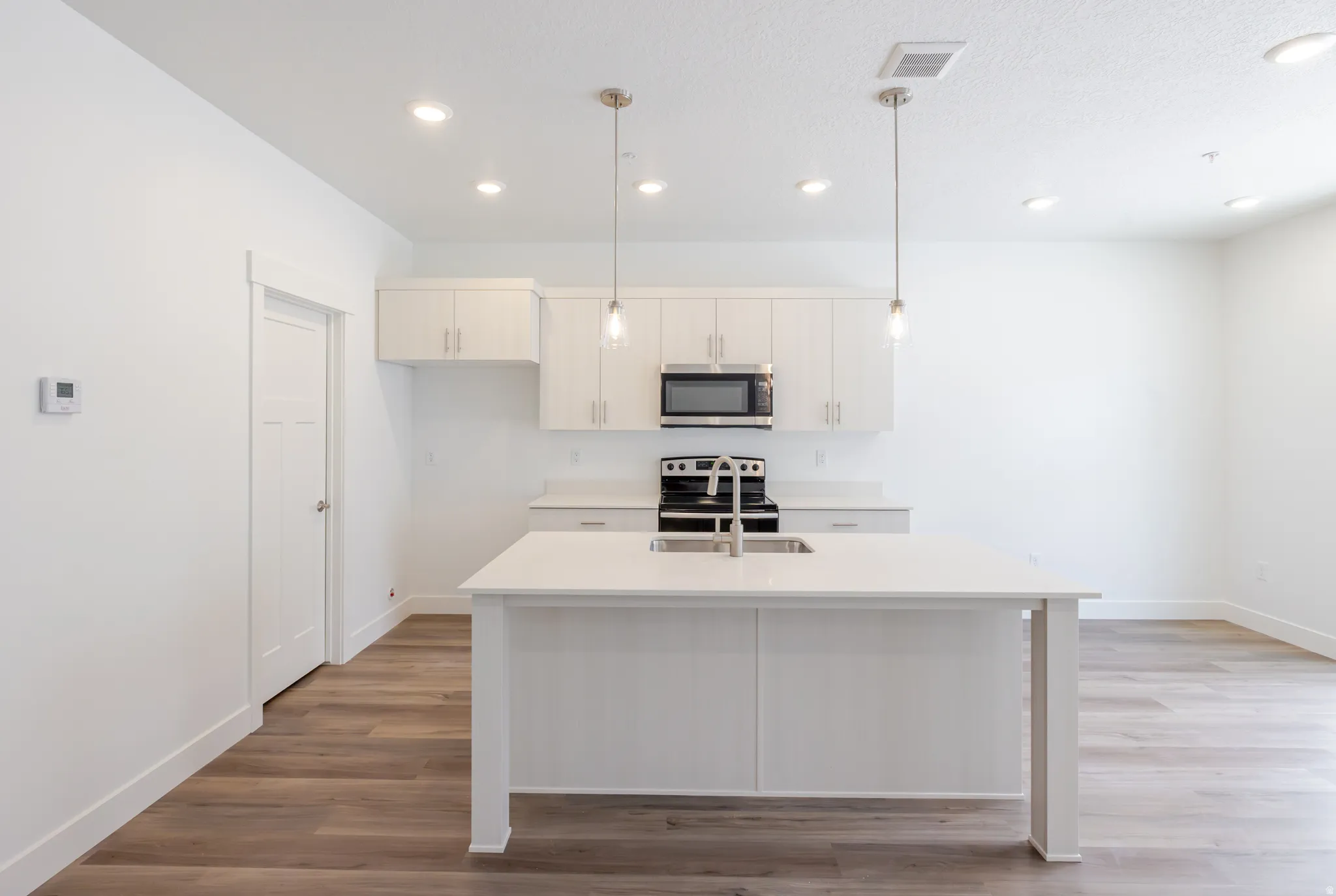 Kitchen featuring light wood-style floors, decorative light fixtures, a kitchen island with sink, and stainless steel appliances