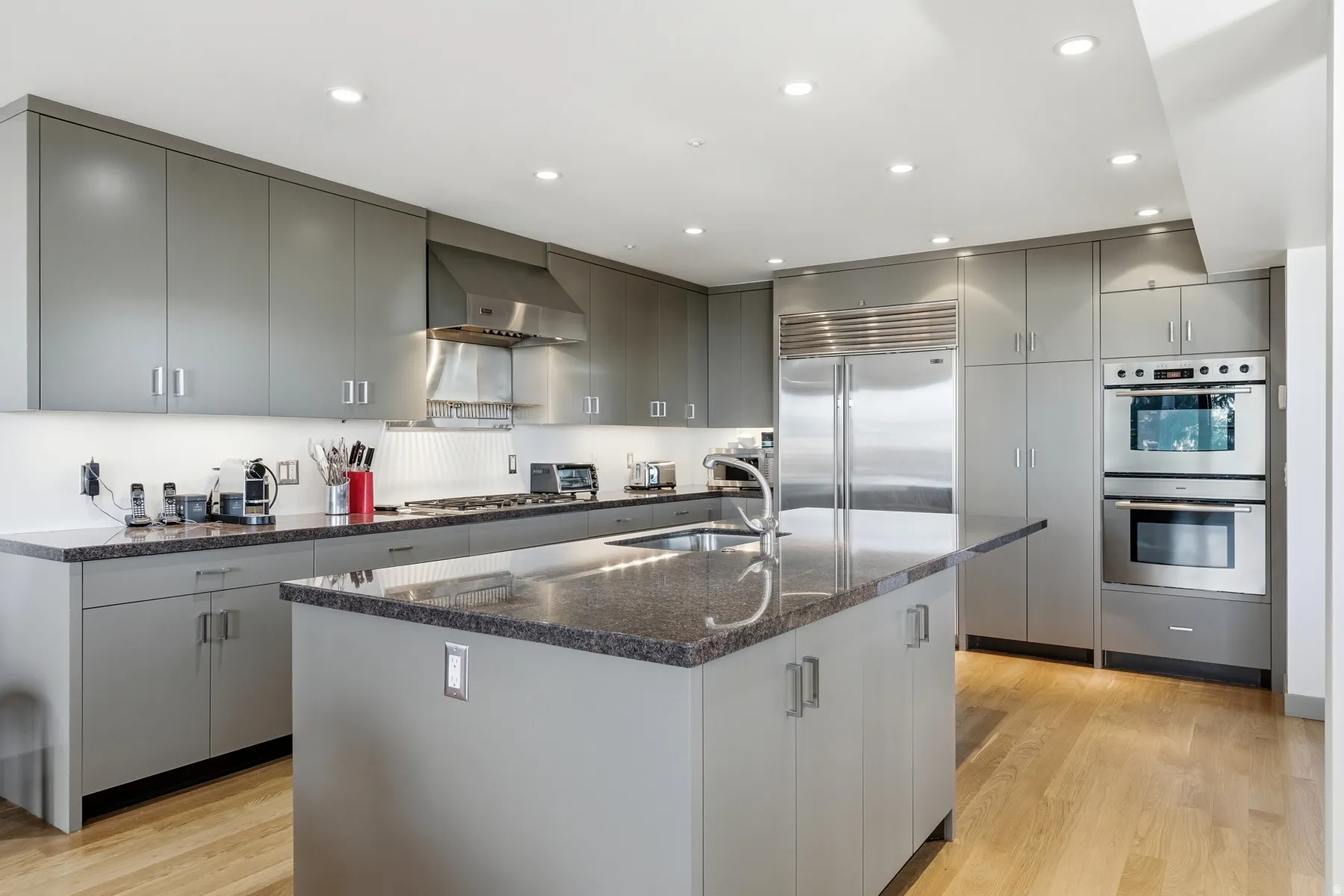 Kitchen with an island with sink, wall chimney range hood, appliances with stainless steel finishes, gray cabinetry, and modern cabinets
