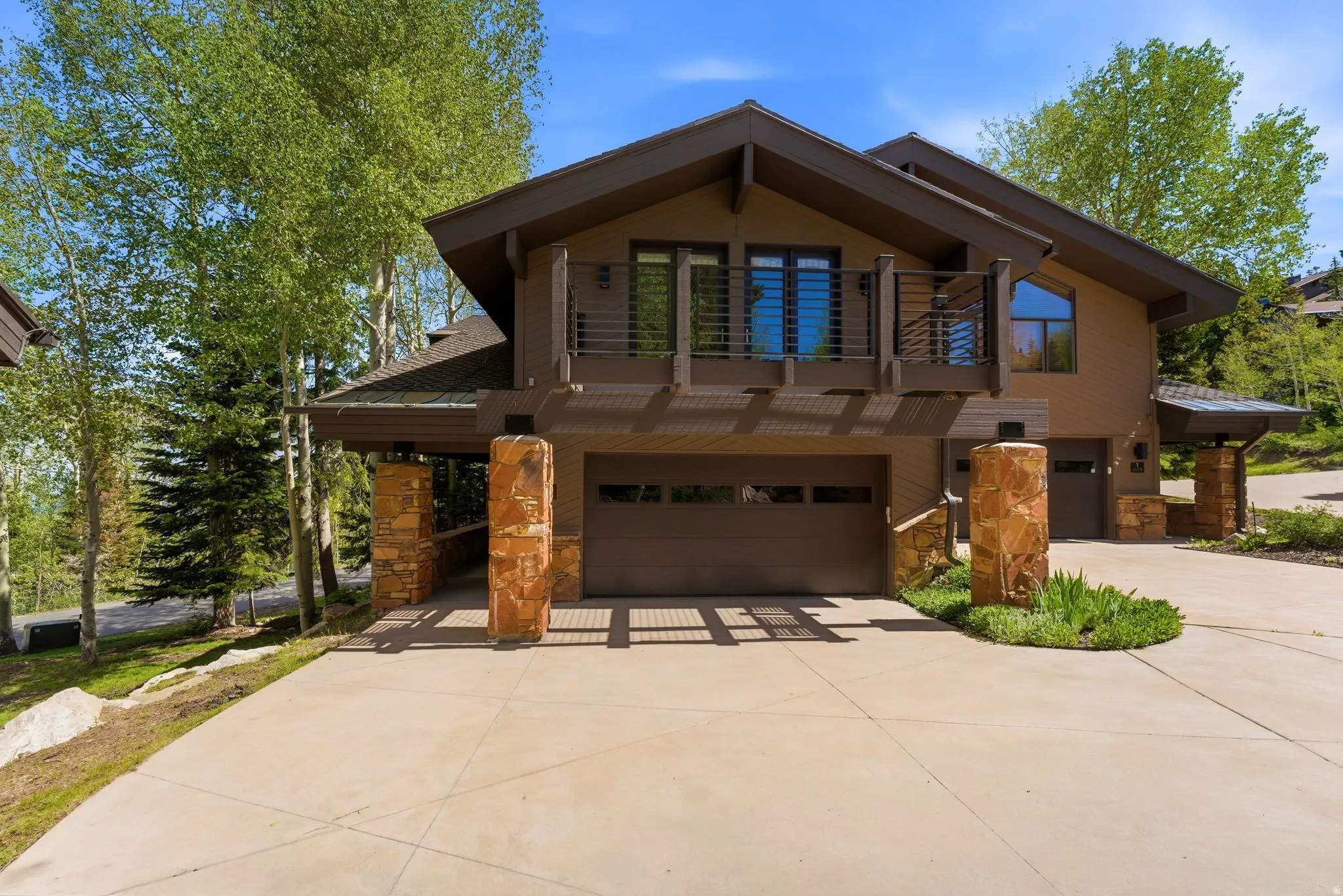 Contemporary residence featuring a multi-car garage, stone-clad architectural columns, a second-story balcony with metal railings, and a distinct roofline