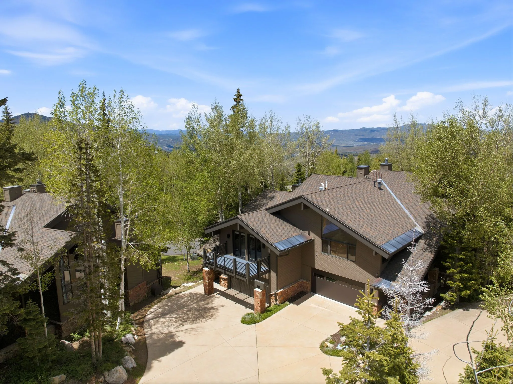 Contemporary mountain residence showcasing a tiered brown shingle roof, integrated garage, and a balcony with dark railings