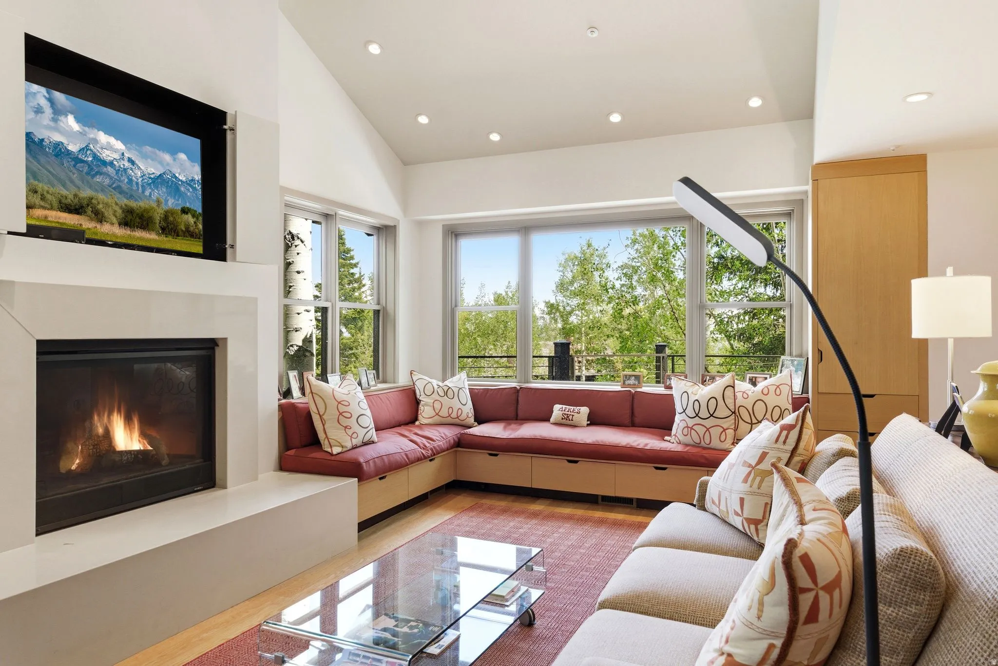 Living area featuring a modern fireplace with a wall-mounted display, vaulted ceilings, recessed lighting, and a built-in window bench with integrated storage