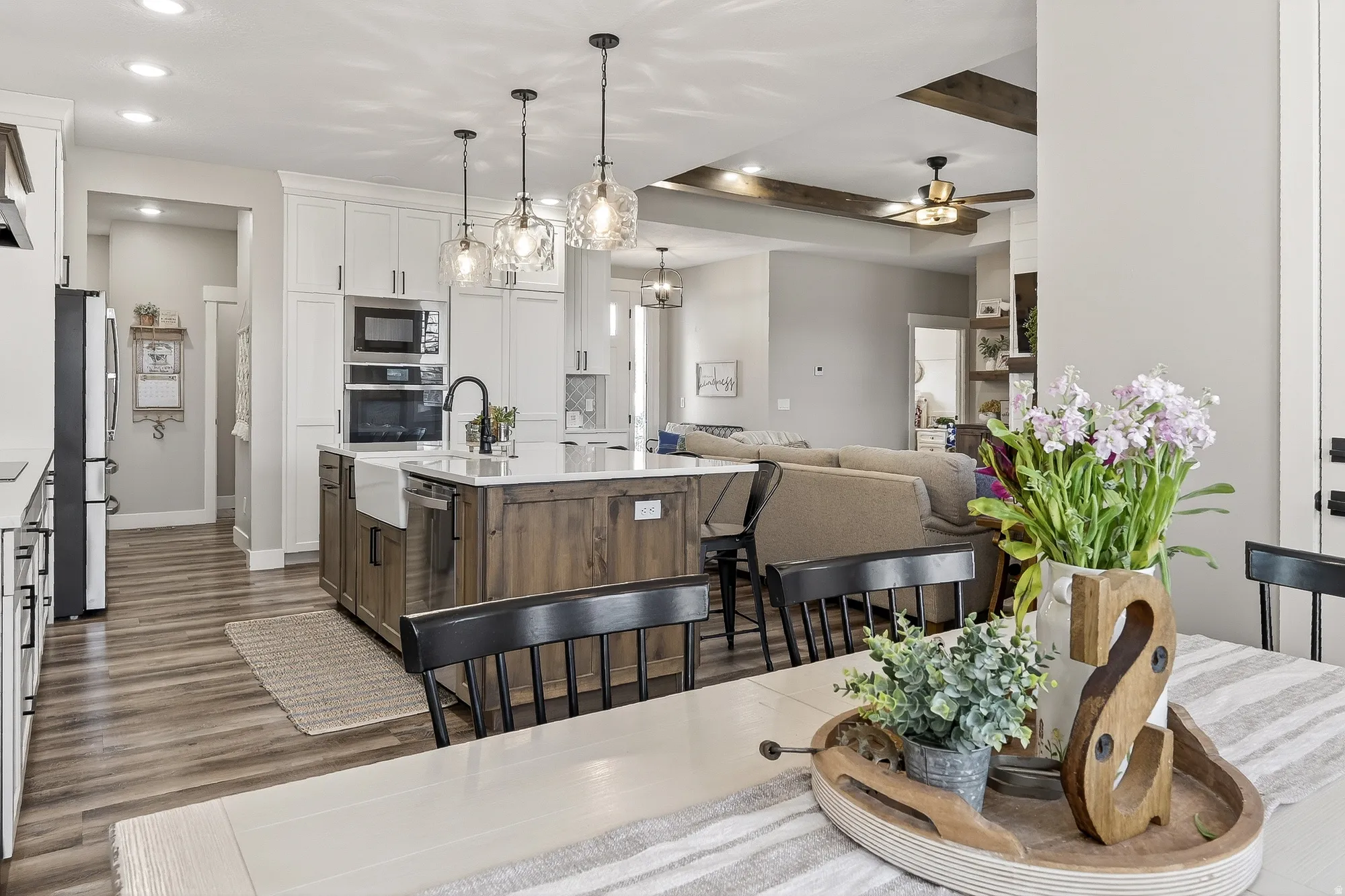Dual tone kitchen featuring two tone cabinetry, open floor plan, decorative light fixtures, stainless steel appliances, and a kitchen island with sink