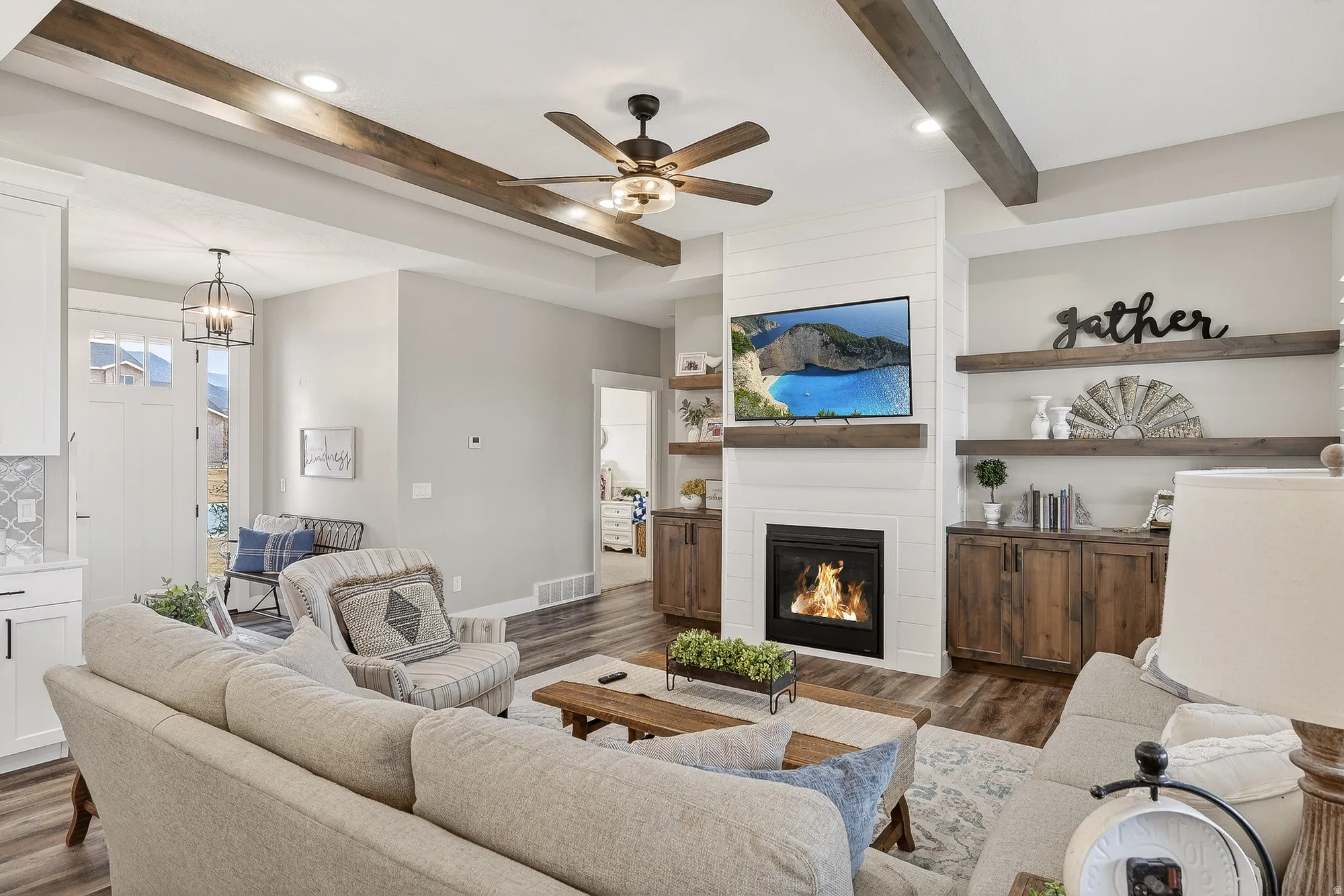 Living room with a ceiling fan, dark wood finished floors, beam ceiling, a fireplace, and suspended lighting