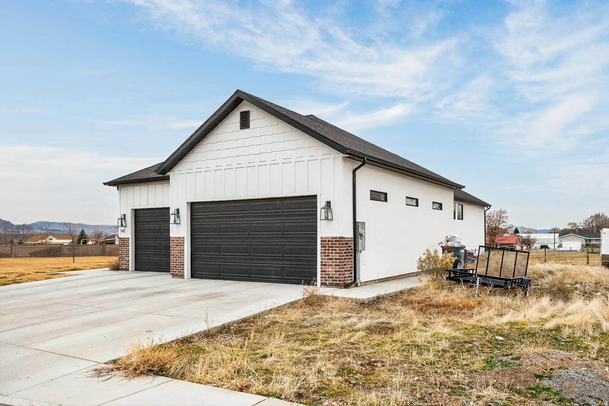 View of side of home featuring board and batten siding, concrete driveway, an outbuilding, and brick siding