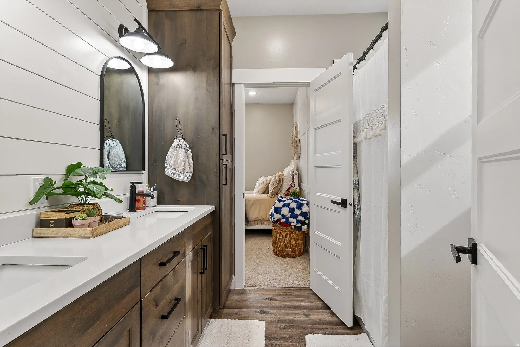 Ensuite bathroom featuring a shower with shower curtain, double vanity, and dark wood-style flooring