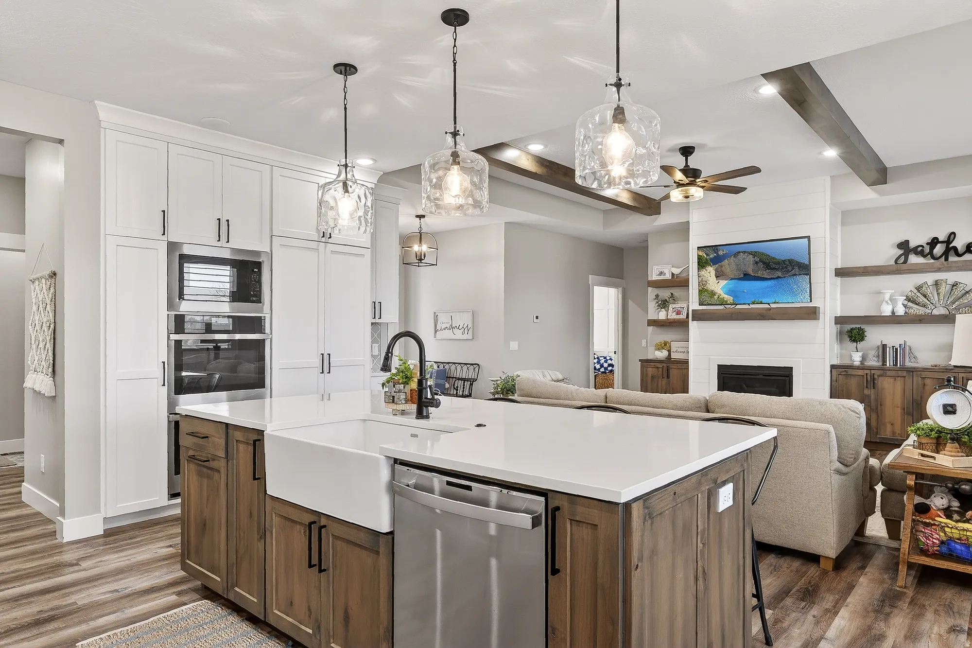 Dual tone kitchen featuring dual tone cabinets, beam ceiling, stainless steel appliances, pendant lighting, and a center island with sink