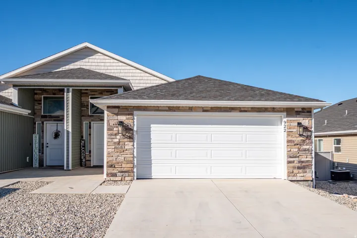 View of front facade featuring stone siding, driveway, roof with shingles, and a garage