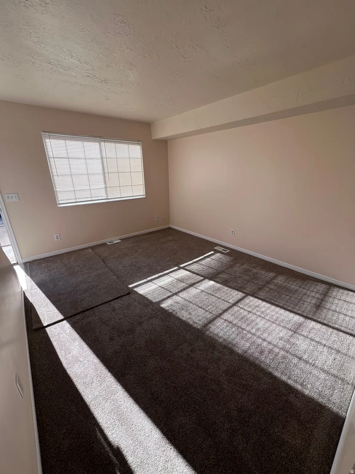 Carpeted spare room with a textured ceiling and baseboards
