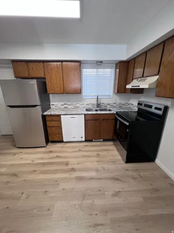 Kitchen with appliances with stainless steel finishes, light countertops, light wood-style flooring, brown cabinets, and under cabinet range hood