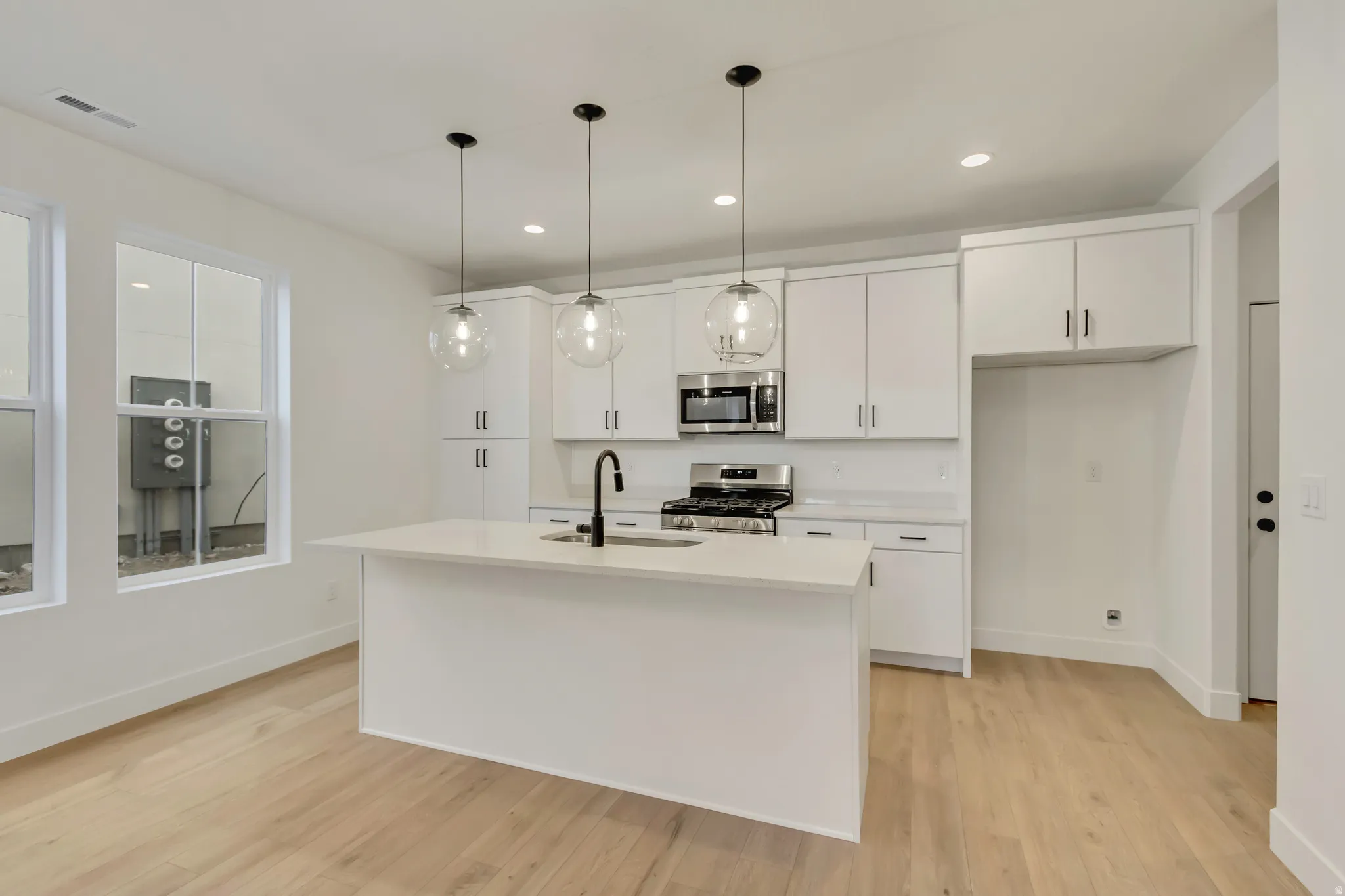 Kitchen with white cabinetry, stainless steel appliances, decorative light fixtures, light wood-style floors, and recessed lighting