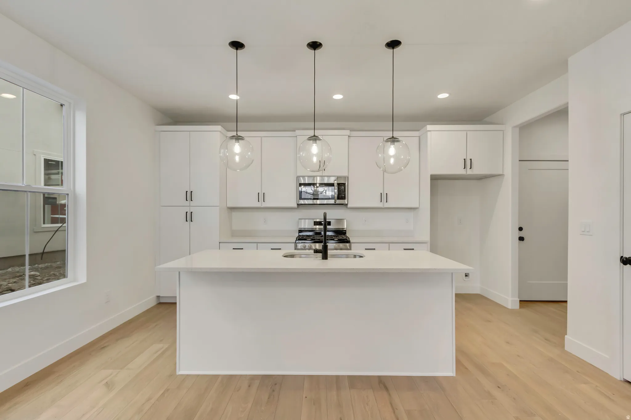 Kitchen with white cabinets, appliances with stainless steel finishes, decorative light fixtures, recessed lighting, and a center island with sink