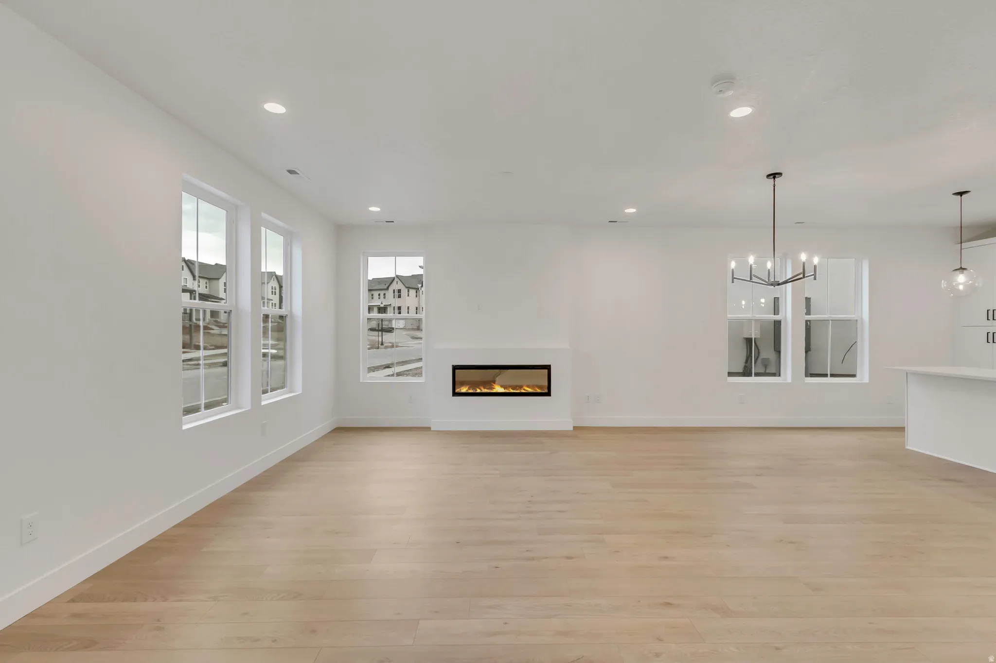 Unfurnished living room featuring a glass covered fireplace, light wood-style floors, recessed lighting, and a chandelier. extra windows in this corner lot