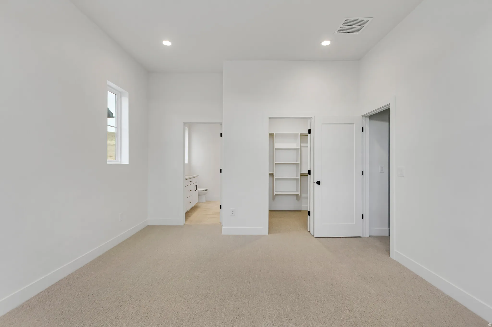 bedroom featuring a walk in closet, light colored carpet, ensuite bathroom, and recessed lighting