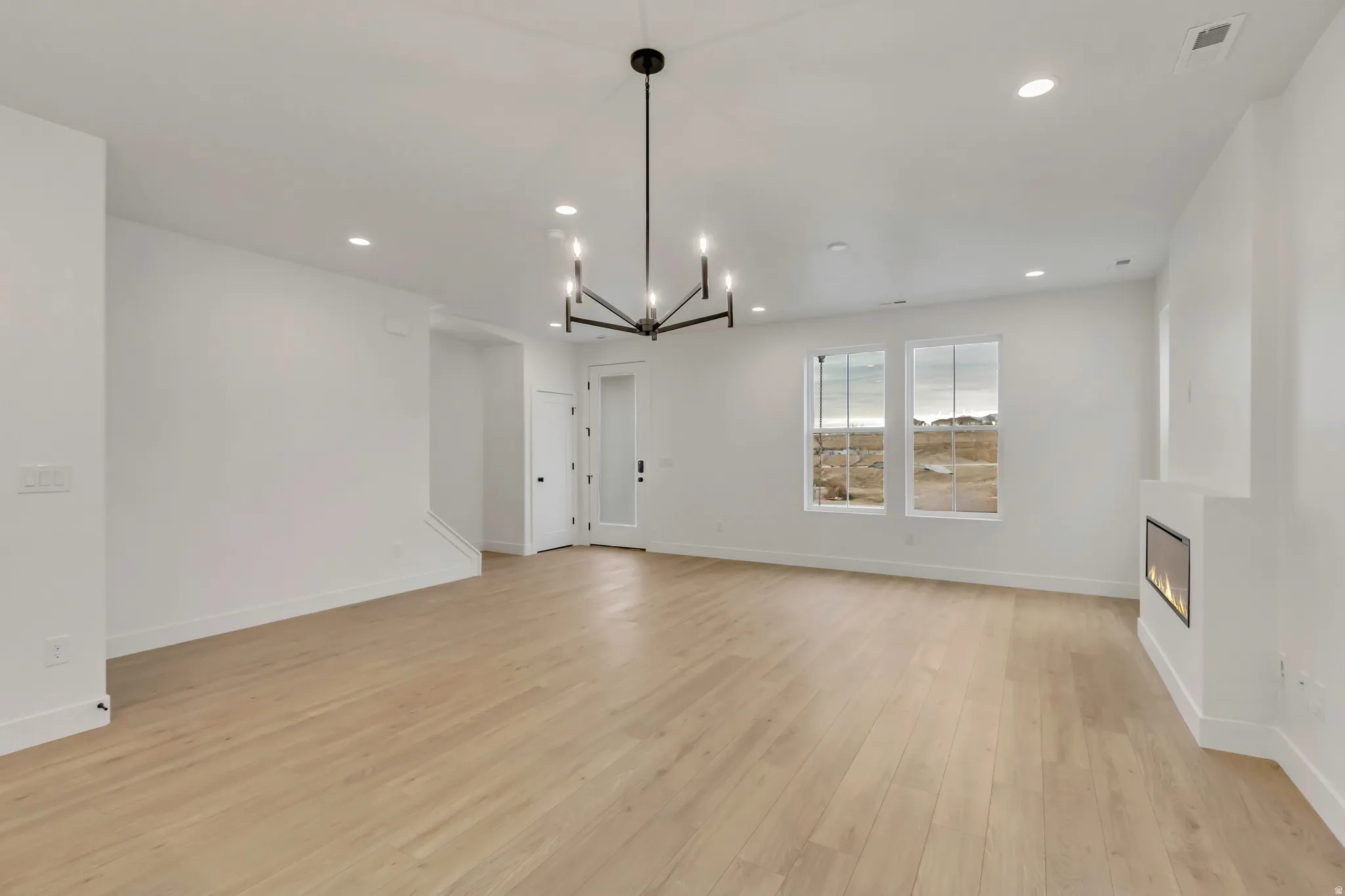 Unfurnished living room with a chandelier, a large fireplace, recessed lighting, and light wood-style flooring