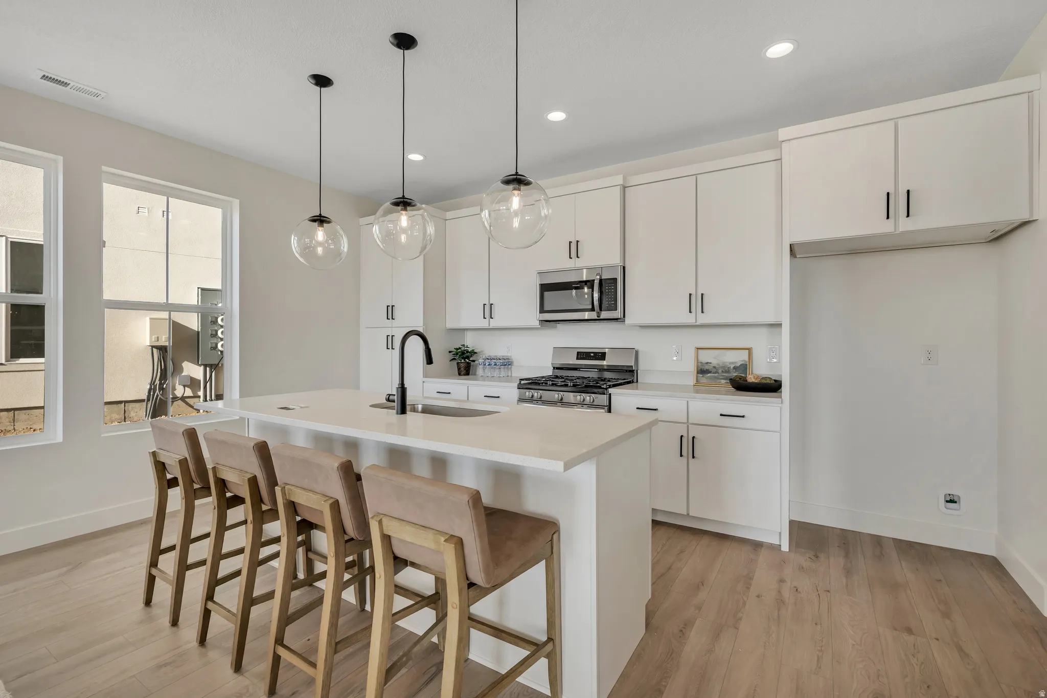 Kitchen with a kitchen breakfast bar, appliances with stainless steel finishes, white cabinets, an island with sink, and pendant lighting