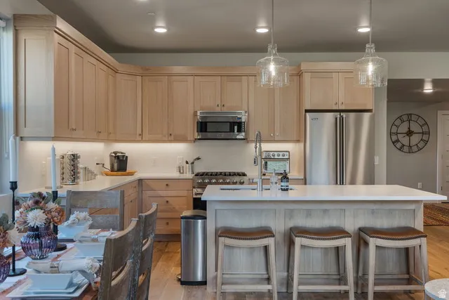 Kitchen featuring light brown cabinets, high end appliances, light wood-style floors, hanging light fixtures, and a breakfast bar area