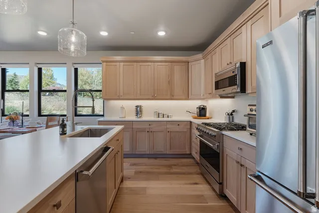 Kitchen featuring premium appliances, decorative light fixtures, light wood finished floors, recessed lighting, and light brown cabinets