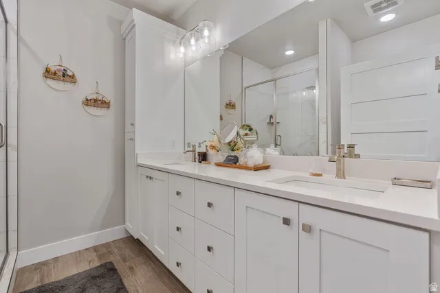 Full bath with double vanity, a marble finish shower, and light wood-style flooring