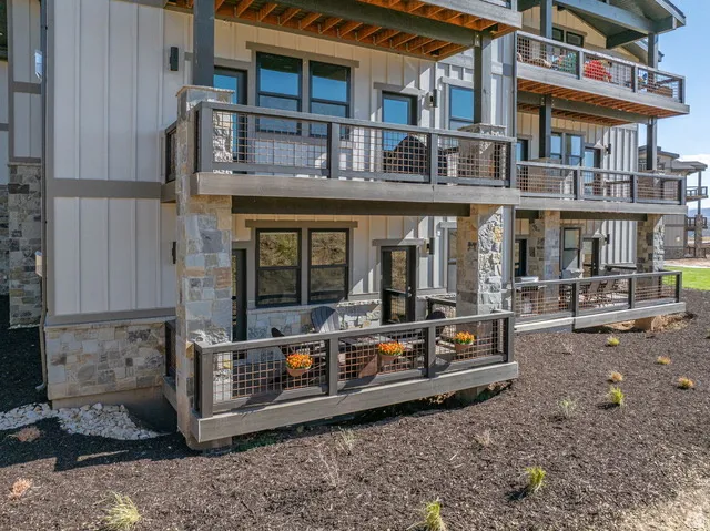 Rear view of property with board and batten siding, stone siding, and a balcony