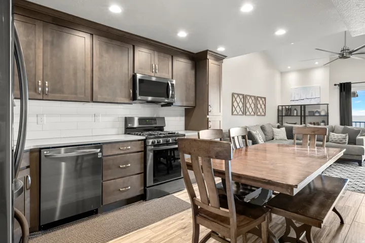 Kitchen with appliances with stainless steel finishes, dark brown cabinetry, a ceiling fan, tasteful backsplash, and light wood-style floors