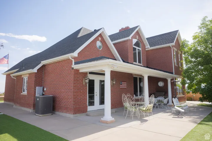 Back of house featuring french doors, brick siding, a shingled roof, covered porch, and a chimney