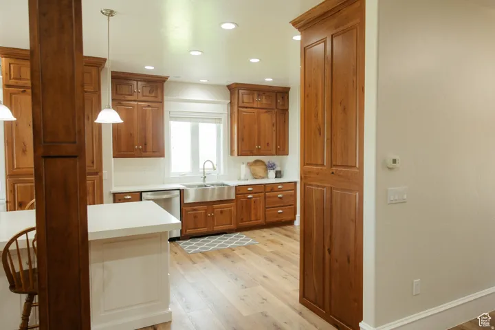 Kitchen featuring light countertops, brown cabinetry, recessed lighting, light wood-type flooring, and stainless steel dishwasher