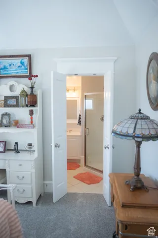 Bedroom with light colored carpet, light tile patterned flooring, ensuite bath, and lofted ceiling