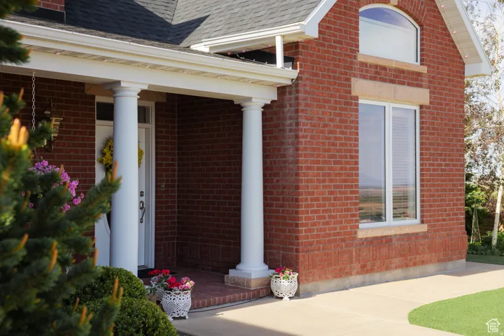 View of exterior entry featuring brick siding, a shingled roof, and covered porch