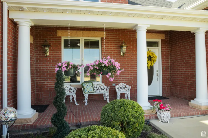 Entrance to property with covered porch, brick siding, and a shingled roof