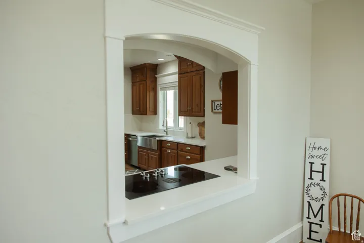 Kitchen featuring light countertops, black electric cooktop, brown cabinetry, dishwasher, and wood finished floors