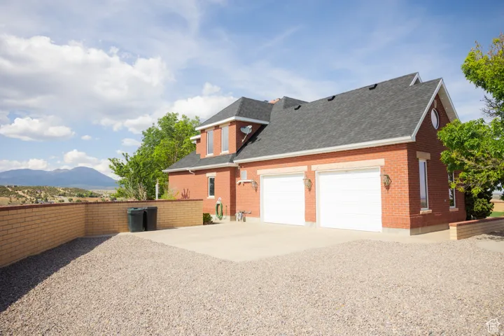 View of side of property with a shingled roof, concrete driveway, brick siding, and an attached garage