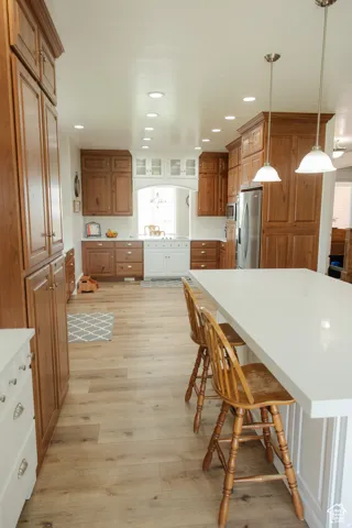 Kitchen featuring a kitchen breakfast bar, brown cabinetry, glass insert cabinets, light wood-style flooring, and recessed lighting
