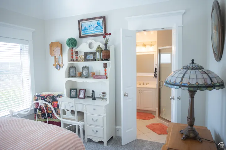 Bedroom with an office area, light tile patterned flooring, and ensuite bath