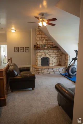 Living room featuring carpet, a ceiling fan, and a stone fireplace