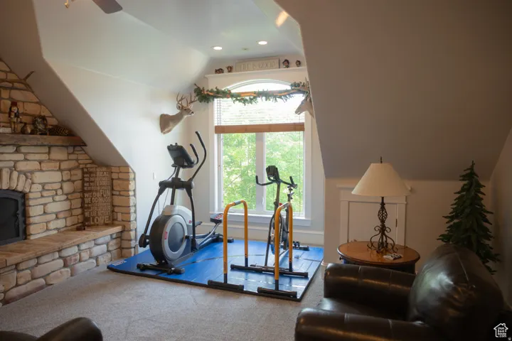 Workout area with vaulted ceiling, carpet floors, a stone fireplace, and a ceiling fan