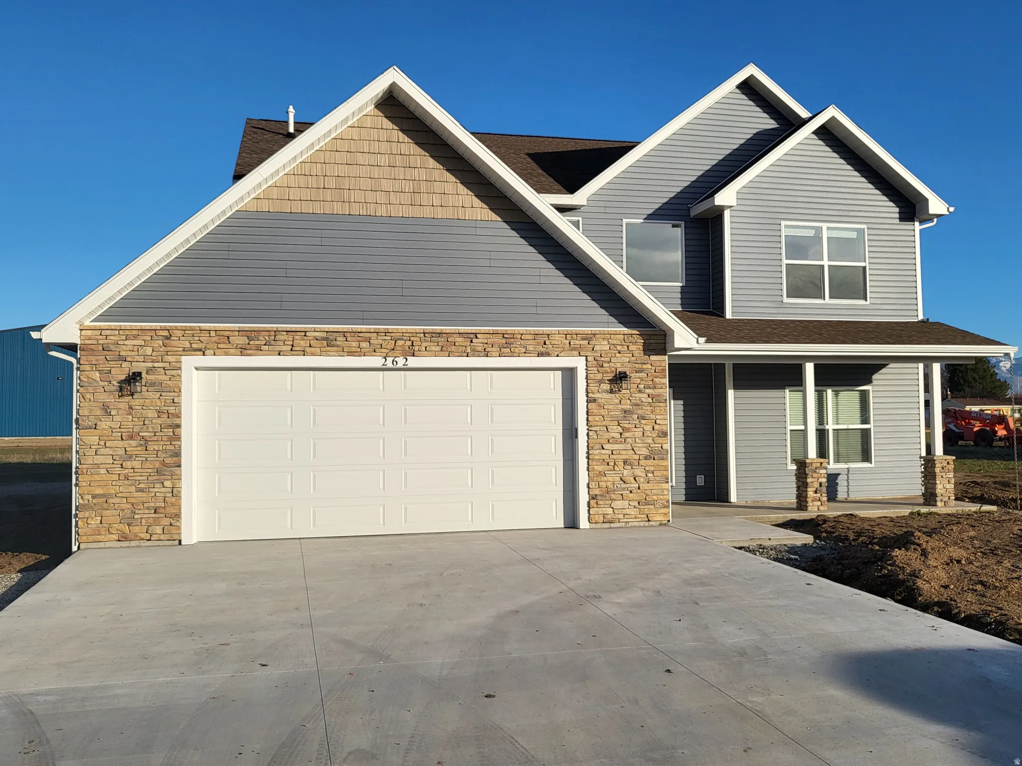 View of front facade featuring stone and vinyl siding, driveway, roof with shingles, and covered porch